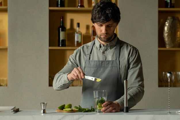 Bartender puts lime and mint leaves in a glass to make a mojito cocktail