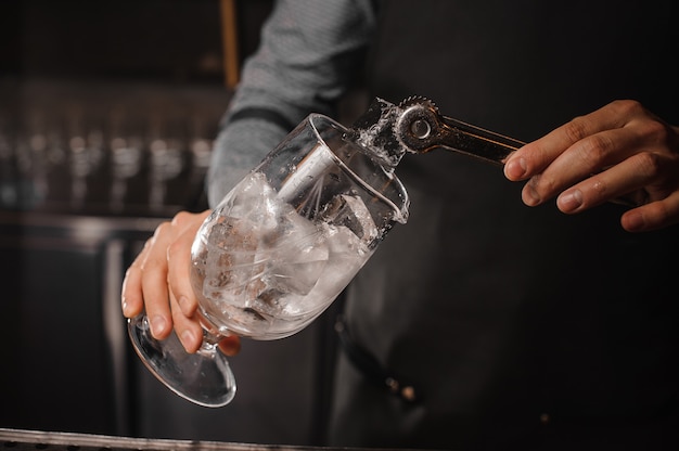 Bartender putting ice cubes into the cocktail glass