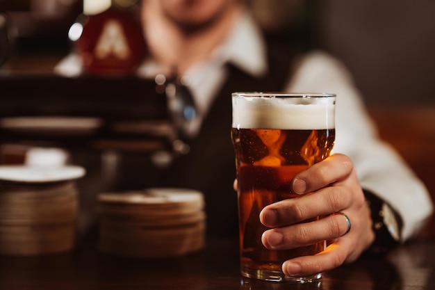 Bartender's hand with a glass of light draft beer with foam in bar