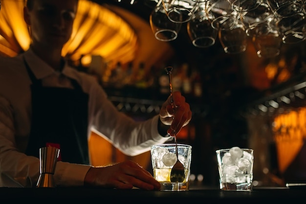 The bartender stirs a spoonful of whiskey with ice in a glass.