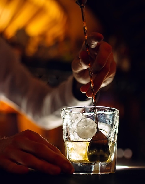 The bartender stirs a spoonful of whiskey with ice in a glass.