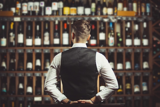 Bartender at wine cellar full of bottles with exquisite drinks