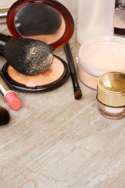 Basic make-up products - foundation, powder and lipstick on wooden background with copy space