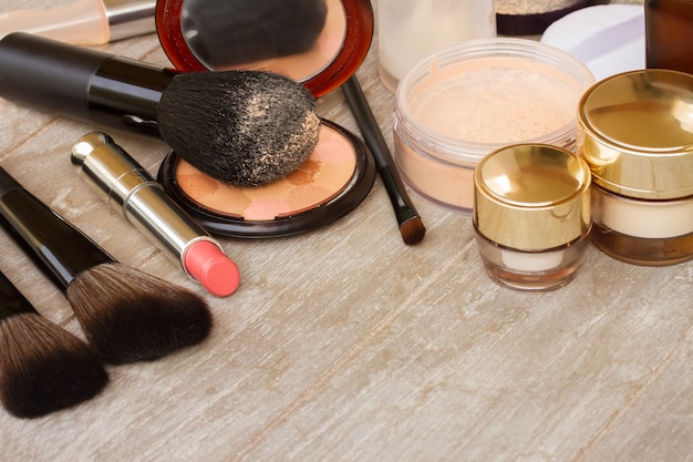 Basic make-up products - foundation, powder and lipstick on wooden table with copy space