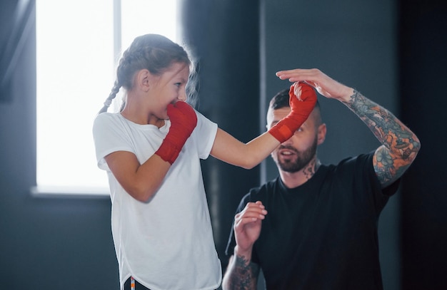 Photo basic punches young tattooed boxing coach teaches cute little girl in the gym