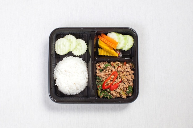 Basil fried rice with minced pork, put in a black plastic box, put on a white tablecloth, food box, Spicy fried pork with basil leaves, Thai food.