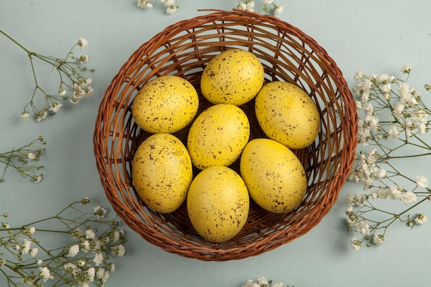 A basket of easter eggs with a bunch of flowers on a blue background.