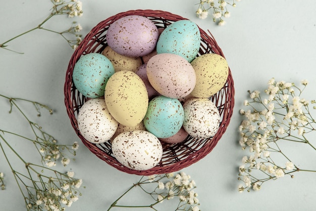 A basket of easter eggs with a bunch of flowers on the table.