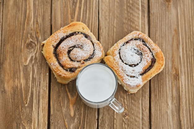 Basket of homemade buns with jam, served on old wooden table with cup of milk