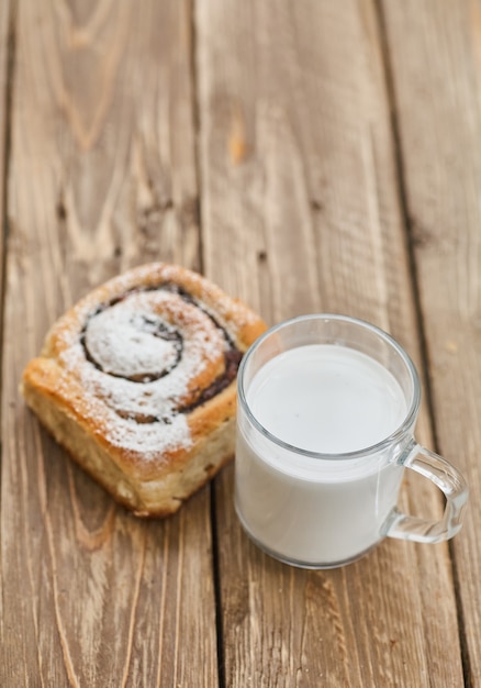 Basket of homemade buns with jam, served on old wooden table with cup of milk