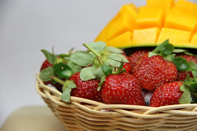 a basket of strawberries and mangoes on the cutting board on white background