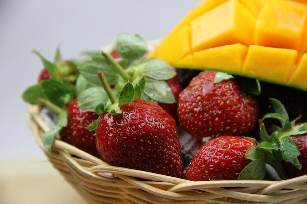 a basket of strawberries and mangoes on the cutting board on white background