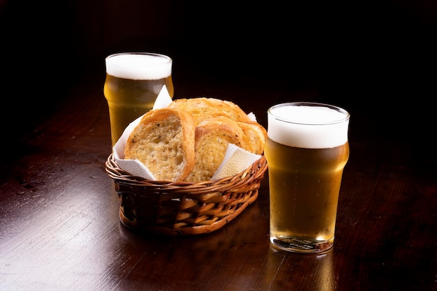 Basket of toasted bread with garlic and two glasses of light beer on wooden table