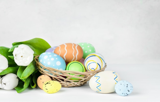 Basket with Easter eggs and a bouquet of white tulips on a light gray background