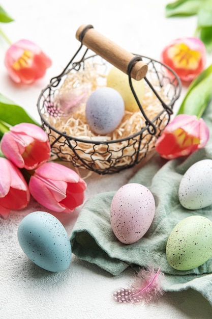 Basket with Easter eggs painted pastel colors and pink tulips on a concrete background