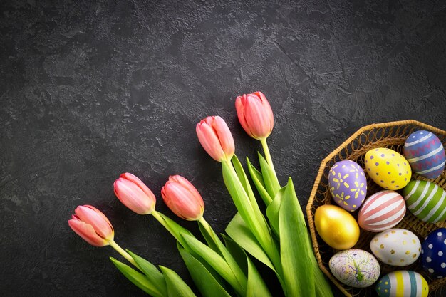 Basket with easter eggs and pink tulips on a dark concrete background