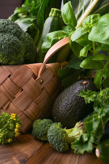 basket with fresh green vegetables on a wooden background. Avocados, broccoli, Cime di rapa other greens. Free space for text. Copy space.