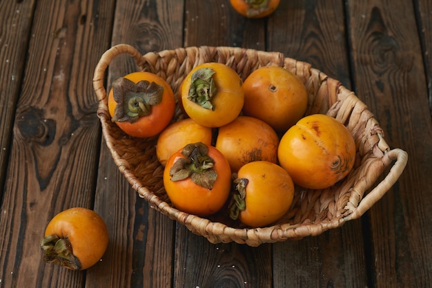 Basket with a harvest of persimmons on a wooden table.