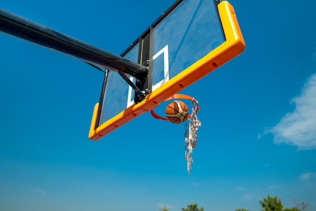 Basketball ball falling through old net blue sky on background