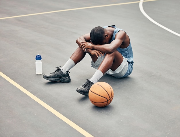 Basketball man sports burnout and game fatigue on court sport training muscle injury from exercise on ground and sad with mistake Sick depressed and african american athlete with competition pain