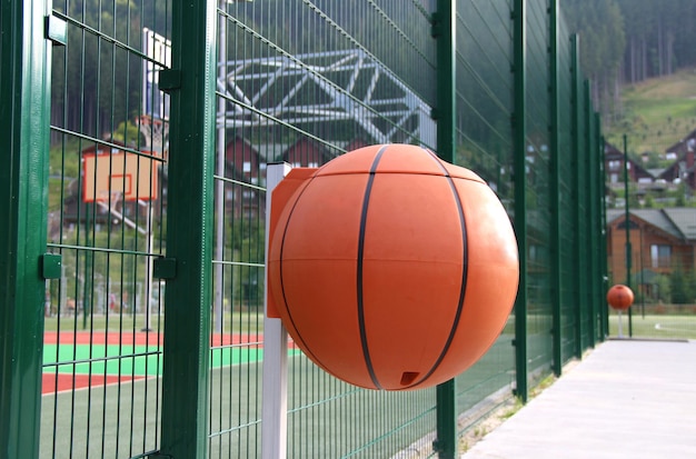 Basketball shaped plastic trash cans at concrete sidewalk around basketball court