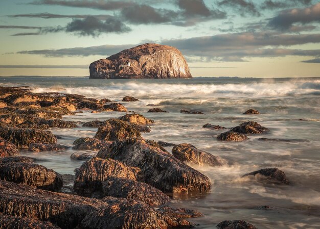 Bass Rock Scotlands east coast from a rocky shore with sun shining on breaking waves Long exposure