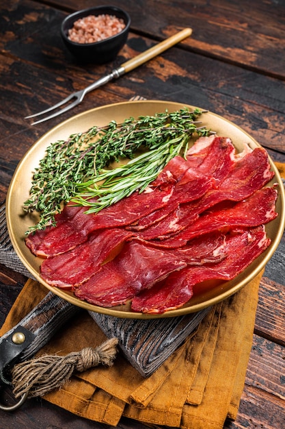 Basturma sliced dried beef meat meat Jerky in steel plate with herbs and spices Wooden background Top view