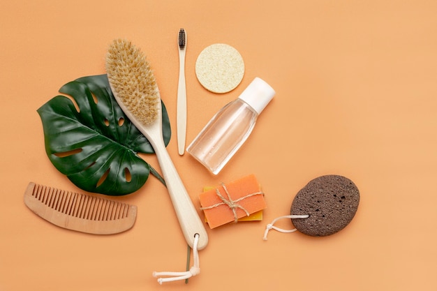 Bathroom accessories with zero waste comb, wooden tooth comb, solid soap, cosmetic jar, wooden comb, sponge with a sheet of monstera on a beige background