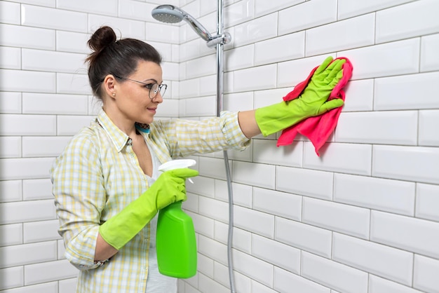 Bathroom cleaning, housewife washing white tile wall with detergent and rag, copy space. Hygiene, purity, cleanliness concept