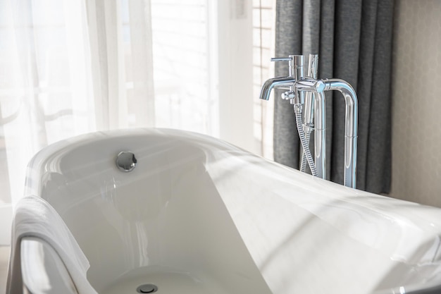 Bathtub in master bathroom in new luxury home, white tub, towel in soft sunlight. Elegant interior