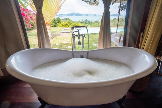 Bathtub with foam bubbles in tropical luxury resort against beautiful ocean background Spa and relaxation concepts