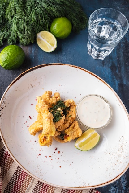 Battered fish on a plate with white sauce and lime Top view