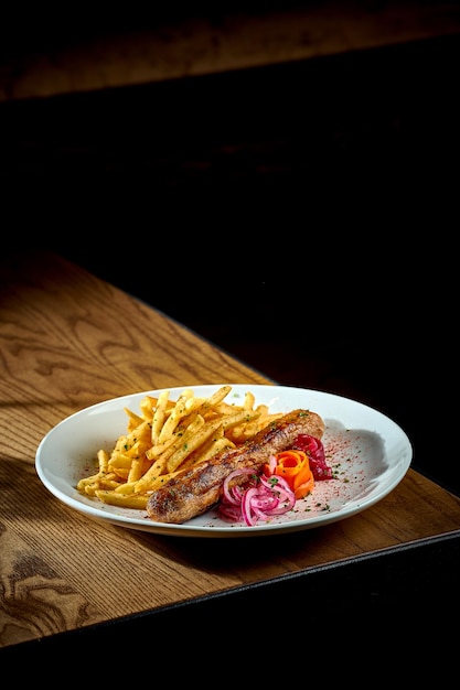 Bavarian meat sausage with a side dish of french fries onions in a plate on a wooden background bratwurst