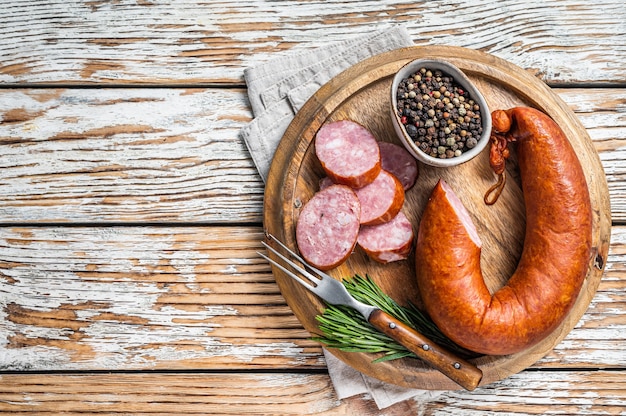 Bavarian Smoked sausage on a wooden board with herbs. White wooden background. Top view. Copy space.