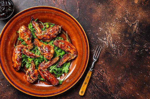 Bbq buffalo chicken wings on a plate with arugula. Dark background. Top view. Copy space.