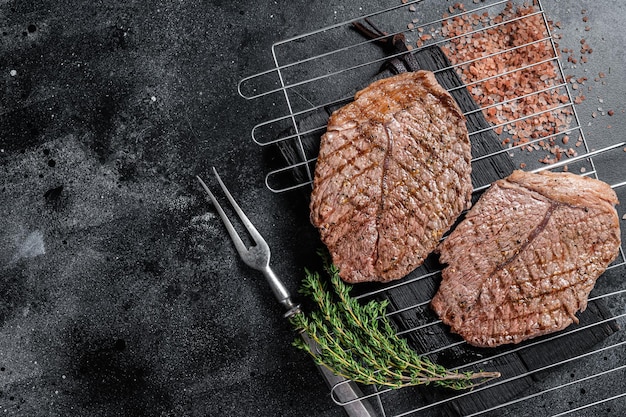 BBQ Grilled beef meat sirloin steaks on grill. Black background. Top view. Copy space.