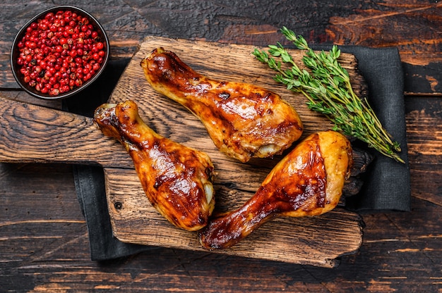 BBQ Grilled chicken drumsticks on a wooden cutting board. Dark wooden background. top view.