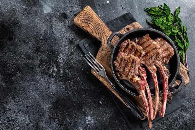 BBq Grilled lamb mutton chops steaks in a pan. Black background. Top view. Copy space.