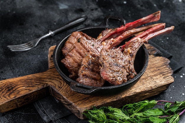 BBq Grilled lamb mutton chops steaks in a pan. Black background. Top view.