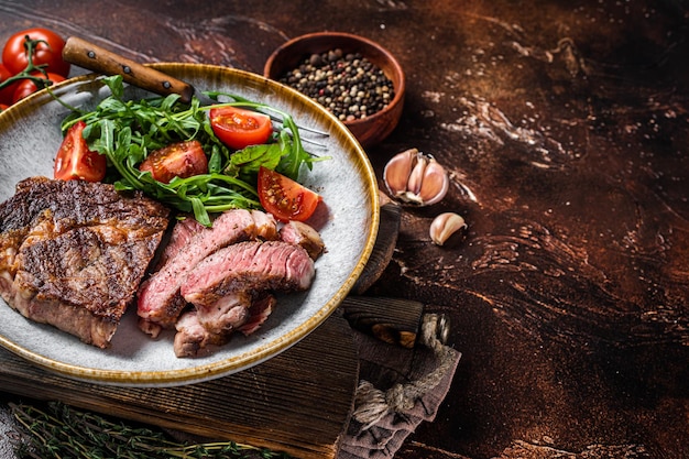 BBQ Grilled rib eye steak fried ribeye beef meat on a plate with green salad Dark background top view Copy space