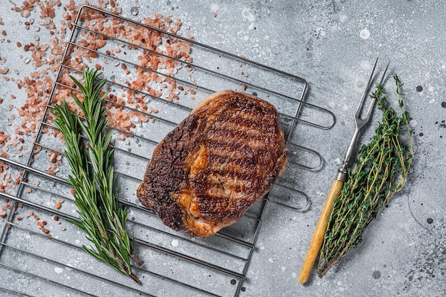 BBQ grilled ribeye steak rib eye beef meat on a grill with herbs Gray background top view