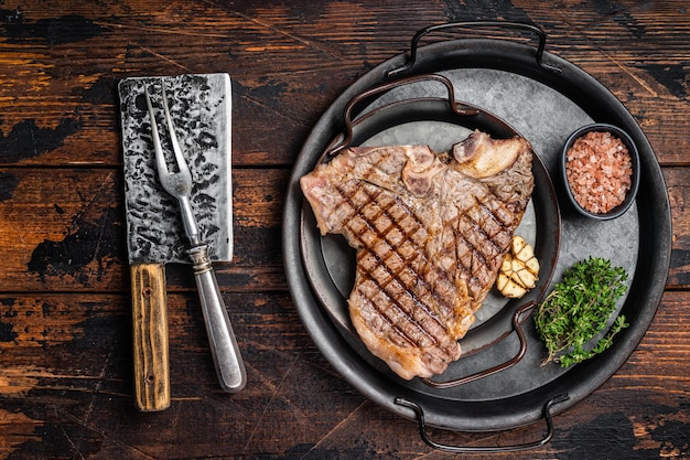 BBQ Grilled Tbone or Porterhouse beef meat Steak on a steel tray with herbs Wooden background Top view