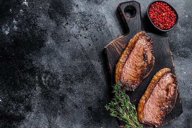 BBQ Grilled top sirloin cap or picanha steak on a wooden cutting board on wooden table. Top view.