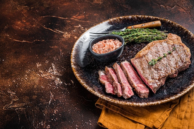 BBQ roast sliced New York beef steak on a plate with thyme and salt Dark background Top view Copy space