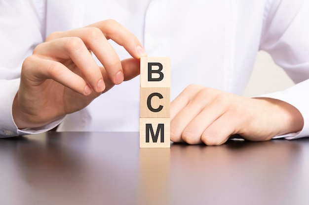 Bcm business continuity management text on cube blocks in businessman hands man in white shirt