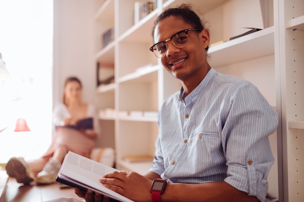 Be happy. Delighted young male person keeping smile on his face while holding book in both hands