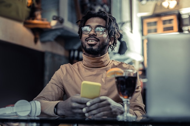 Be positive. Handsome male person keeping smile on his face while spending break in cafe