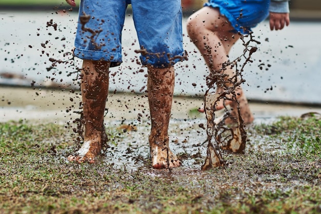 Be young make a mess Low angle shot of two unrecognizable children jumping around in mud outside during a rainy day