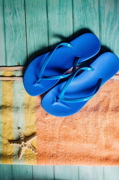 Beach accessories on blue wooden floor. Top view. Towel and flip flops