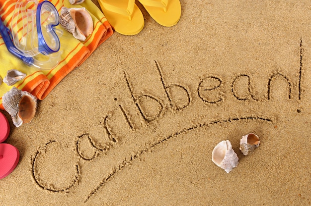 Beach background with towel and flip flops and the word Caribbean written in sand 